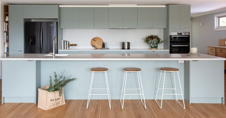 Soft green kitchen cabinetry with a large island bench and bar stools with timber seat
