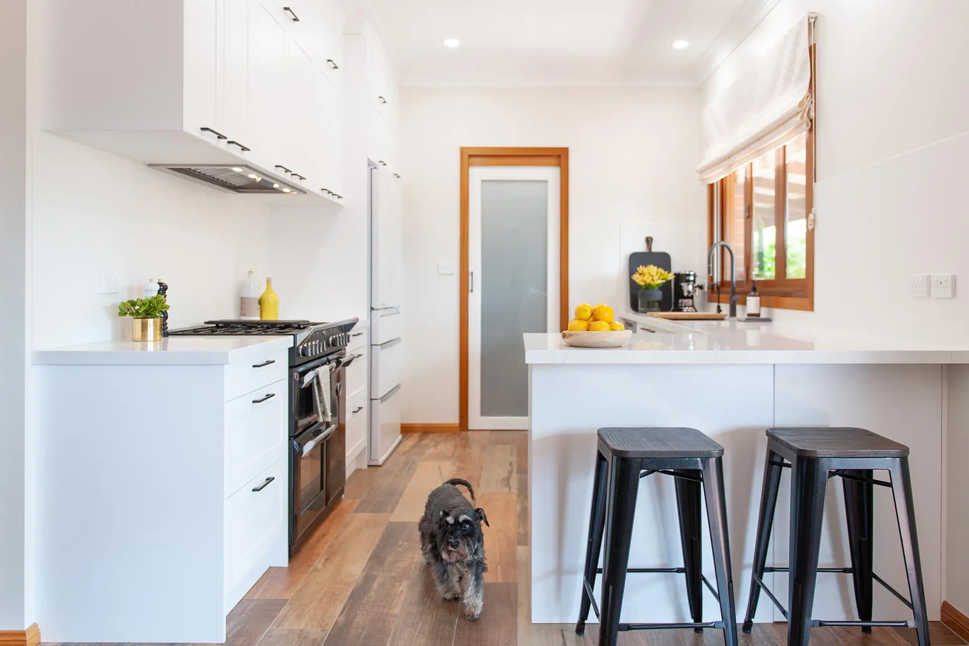white kitchen cabinetry in galley shaped kitchen with timber windows and doorway