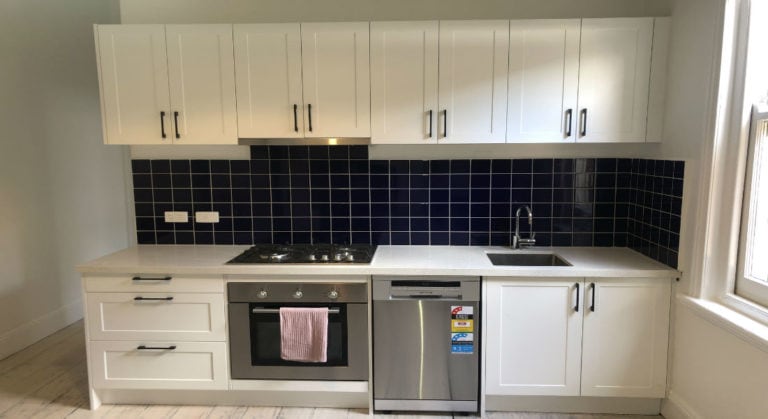 Kitchen with contrasting colours along with white cabinet and black tiled splashback