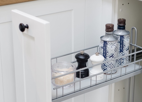 Pull out spice rack in white kitchen cabinetry featuring oils and pepper and salt