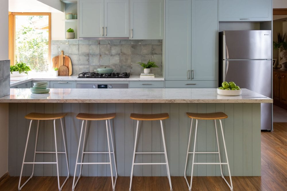 Galley kitchen featuring green coloured cabinetry with long island bench with timber and white stools