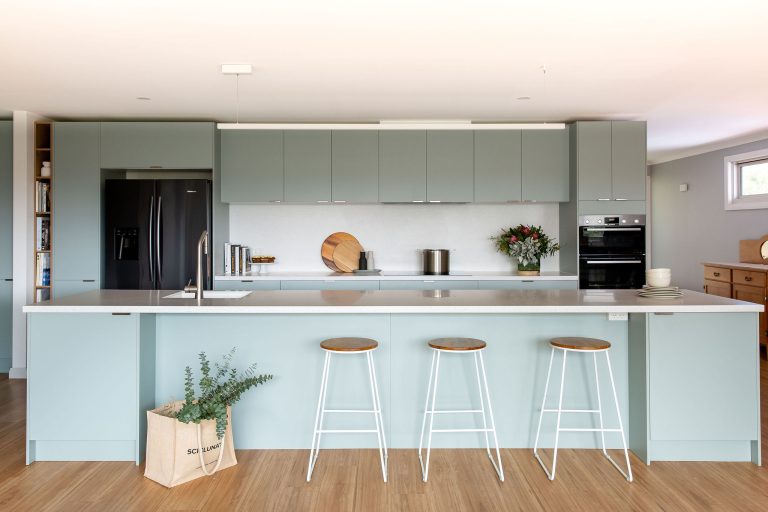 Soft green kitchen cabinetry with a large island bench and bar stools with timber seat