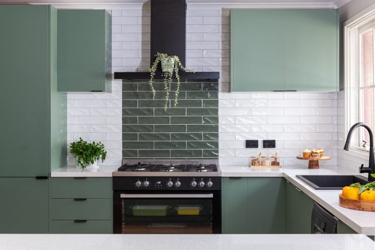 U shaped kitchen featuring sage green cabinetry with white stone benchtops and white and green tiled splashback