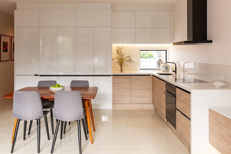 U shaped kitchen with white cabinetry to the ceiling and rural oak timber laminate underbench cabinetry with black rangehood and dining table