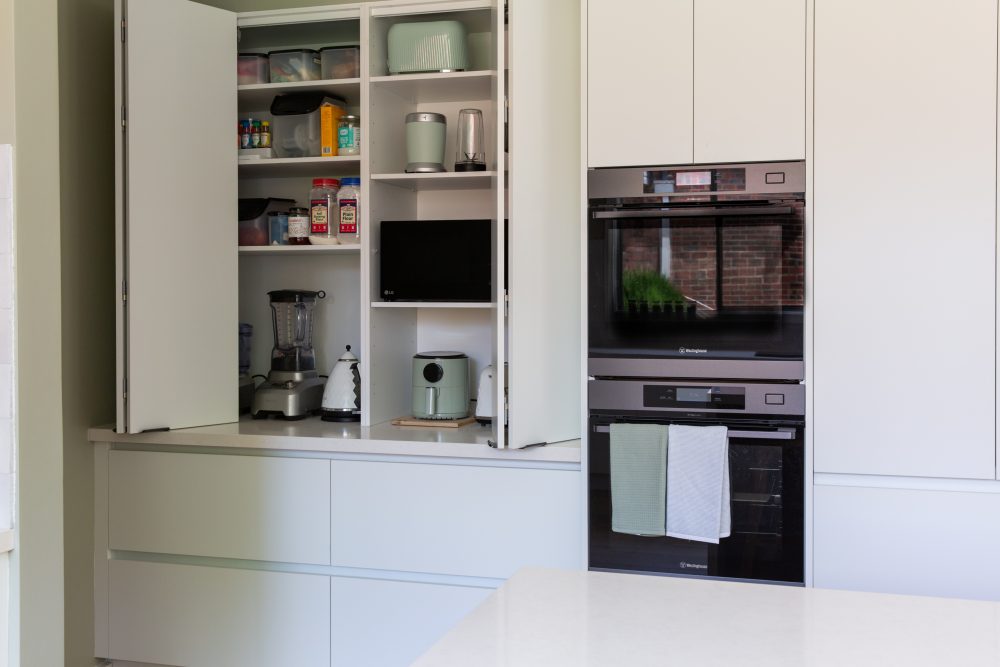 Kitchen appliance cabinet with bifold doors in white next to double oven cabinetry