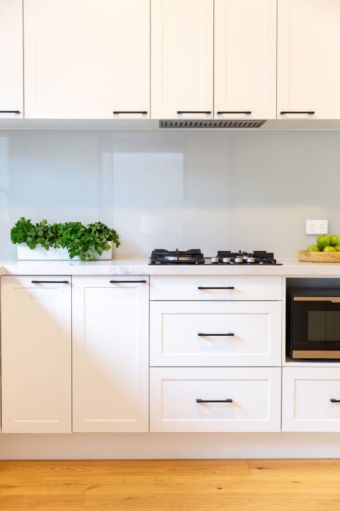 Kitchen cabinetry in white hampton style with black bar handles and white stone benchtops with herbs and fruit