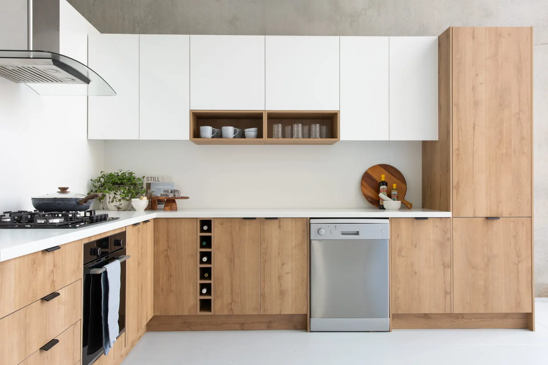 Timber kitchen cabinetry and white overhead cabinetry with timber open shelves in u shape kitchen with dishwasher, oven and plants and cutting boards on benchtops for kitchen styling