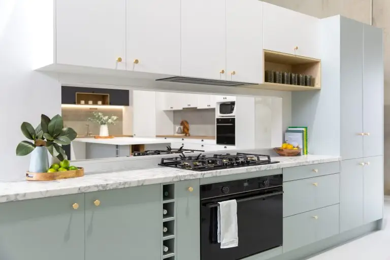 Galley Kitchen in pale green cabinetry with brass round knobs and wine rack with overhead timber laminate shelf