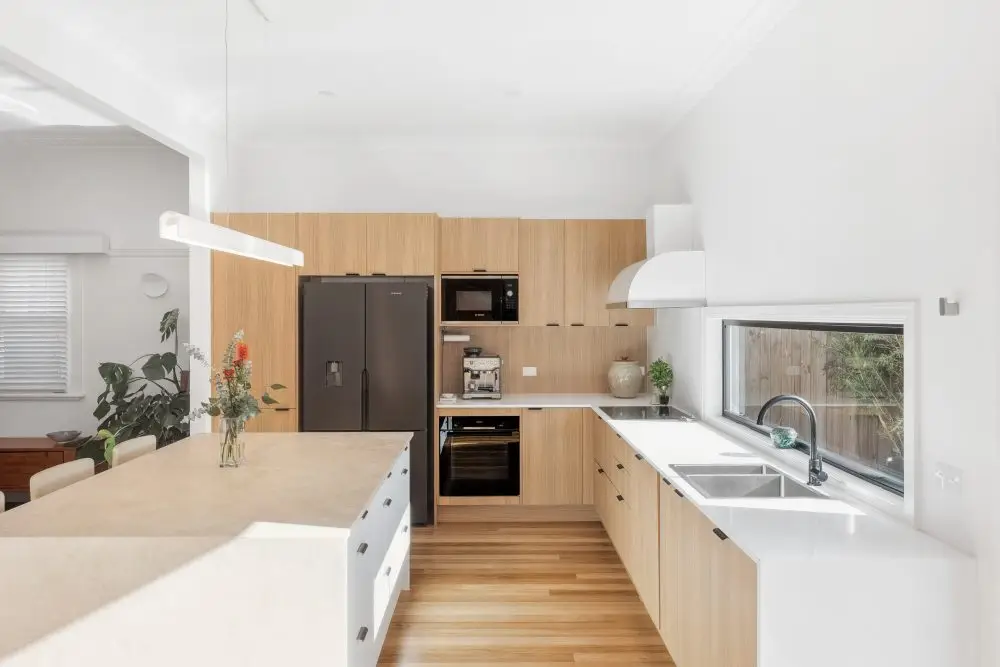 Galley kitchen featuring oak type laminate and white kitchen cabinetry with open plan window onto garden