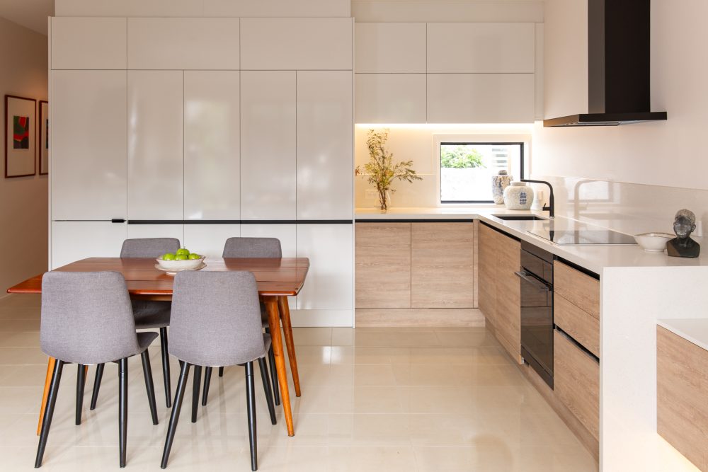 L shaped kitchen featuring white gloss and timber look cabinetry with four seater dining table