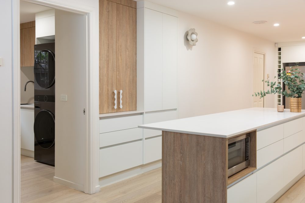White and oak coloured timber kitchen featuring handle free cabinetry and island bench featuring microwave cabinet