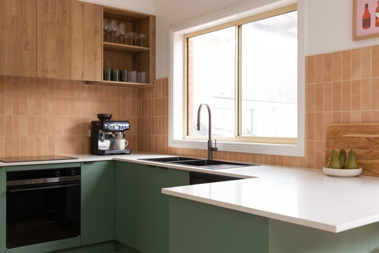 Green kitchen cabinetry in a u shape kitchen with timber overhead laminate cupboards and open shelves displaying glassware