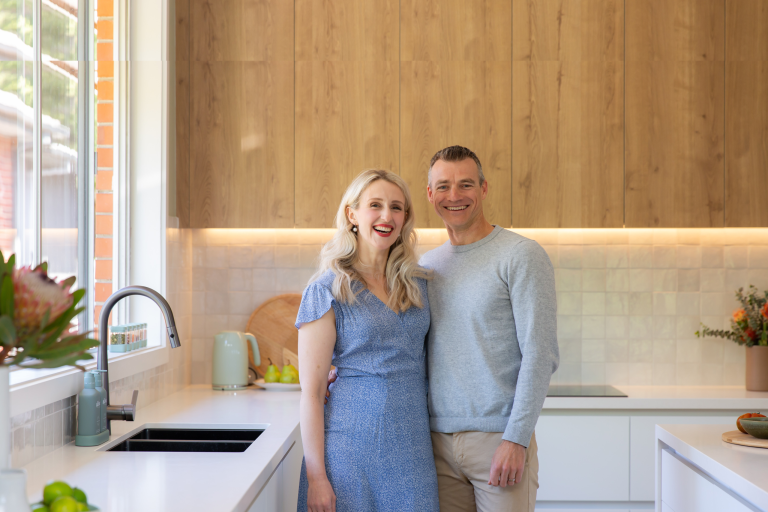 A female and her partner standing in a white kitchen with oak timber cabinetry overheads