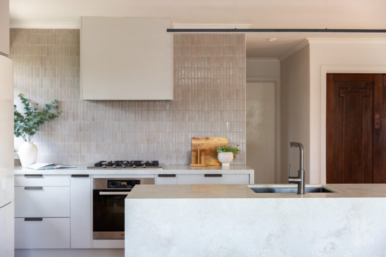 Oyster grey kitchen cabinetry in a galley kitchen featuring stainless stell oven and cooktop and plant and chopping board on bench