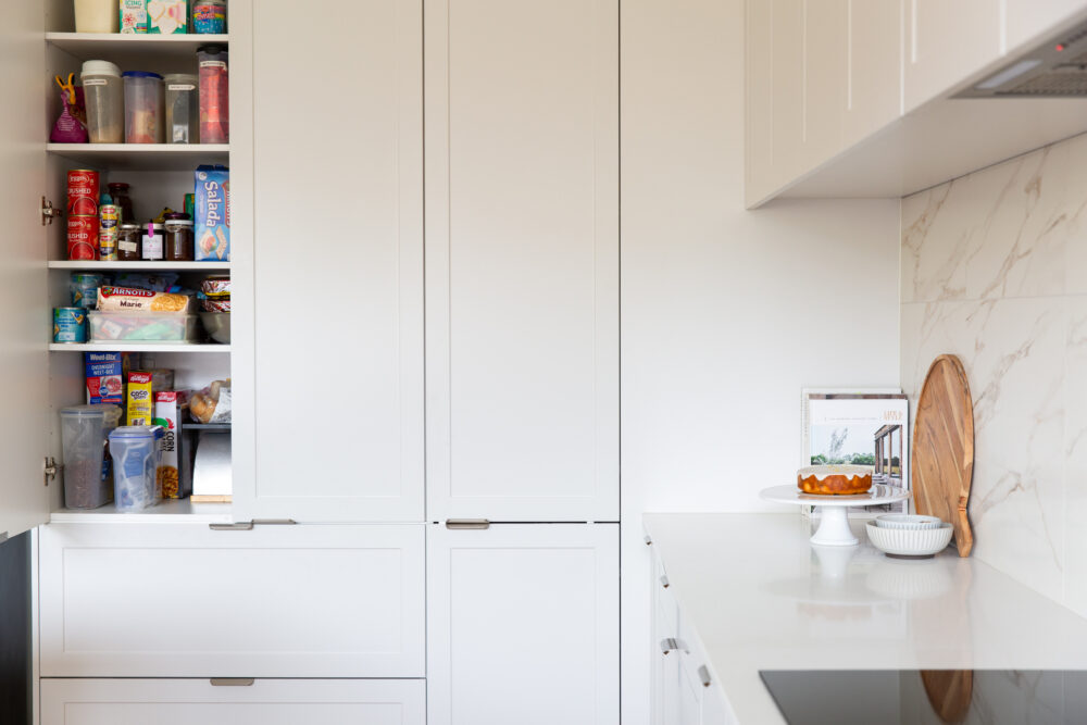Kitchen pantry in light grey cabinetry featuring pantry items and large pot drawers below