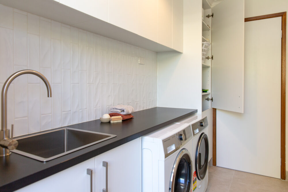 White laundry cabinets in a row with black benchtops and washer dryer side by side