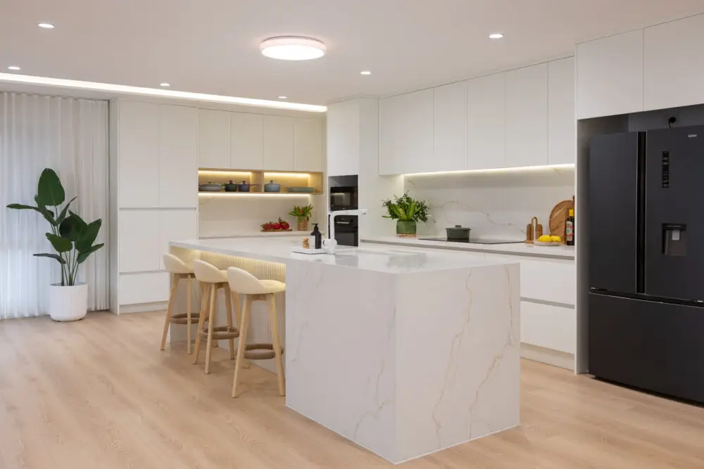 Large open plan kitchen featuring white kitchen cabinetry with standalone stone island bench with waterfall ends and three stools at island