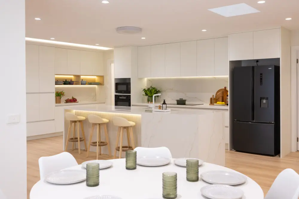 Large galley style kitchen with three bar stools at an a large island bench made from stone