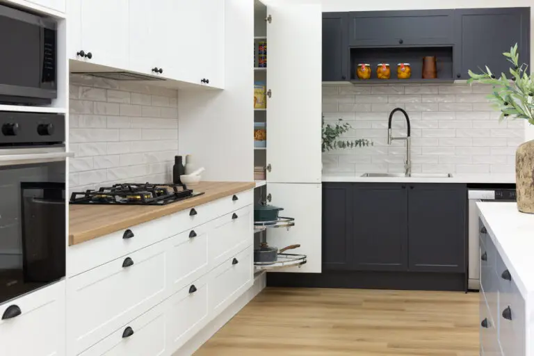 Galley kitchen in a showroom displaying white and dark shaker style cabinetry with pantry and pull out corner unit with pots