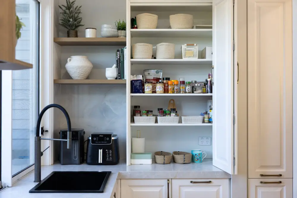 Butlers pantry featuring appliance cupboard in white shaker style cabinetry with pantry items, herbs and spices next to corner shelves in oak and black airfryer next to black sink and gooseneck tap