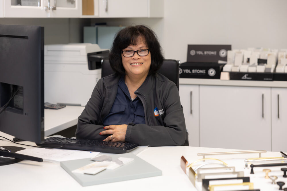 Lady in grey jacket sitting at a desk displaying kitchen samples and handles to design a kitchen in a kitchen showroom
