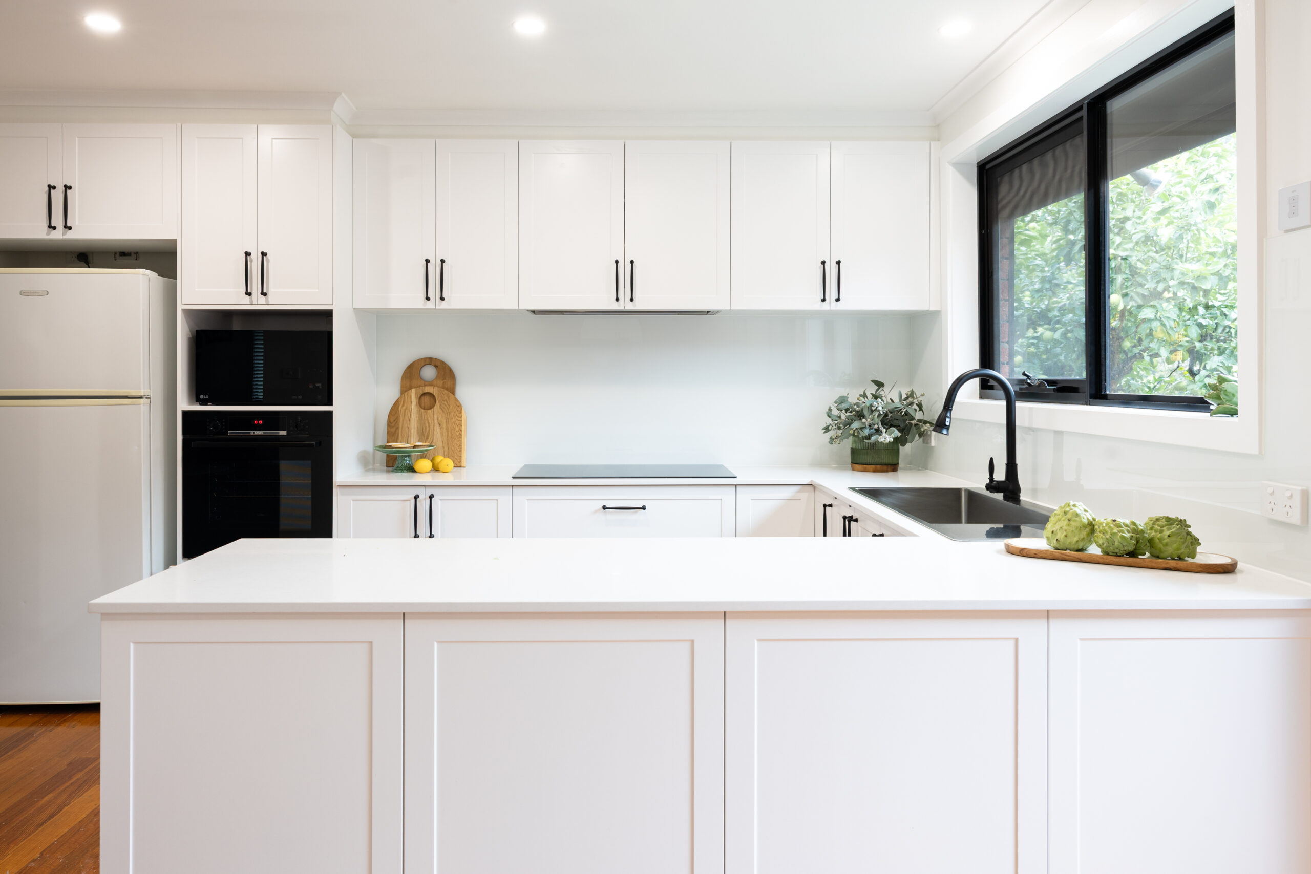 White shaker style cabinetry in this u shaped kitchen with black windows, black handles and black oven and microwave