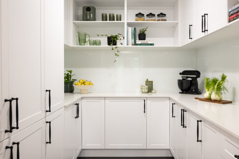 U shaped butlers pantry with white shaker style cabinetry with black handles and open shelves displaying green glasses, plant and styling items on stone benchtops