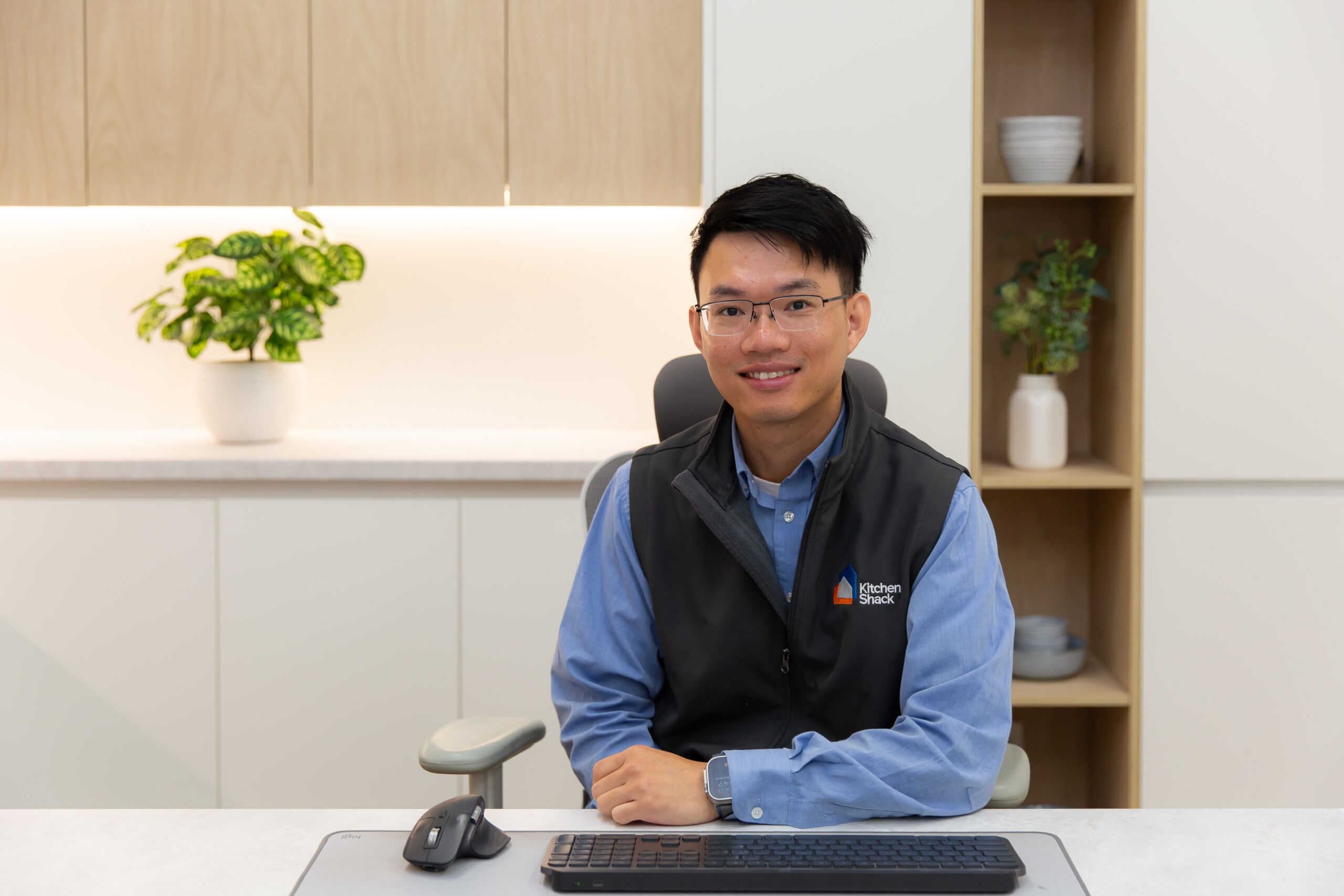 Kitchen Shack kitchen designer sitting at desk with blue shirt and vest with kitchen shack logo in kitchen display