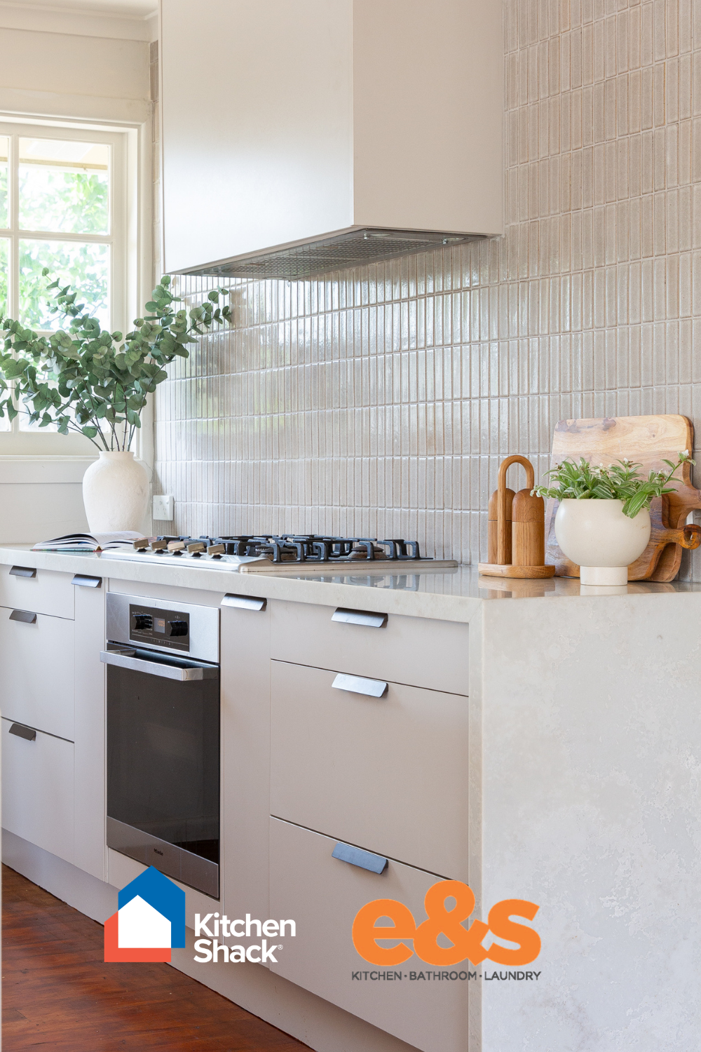 White galley style kitchen displaying kitchen cabinetry with black pull handles and underbench oven in black and stainless steel and overhead rangehood