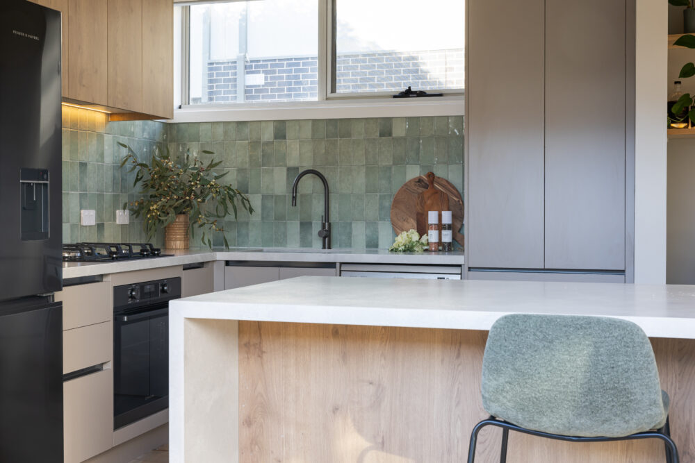 Kitchen displaying pantry in beige coloured cabinetry with green tiled splashback and chopping board and plants decorated on benchtops