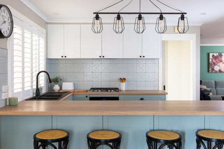 U shape kitchen featuring green underbench kitchen cabinetry and white overheads with a row of five lights above with black sink tap and appliances