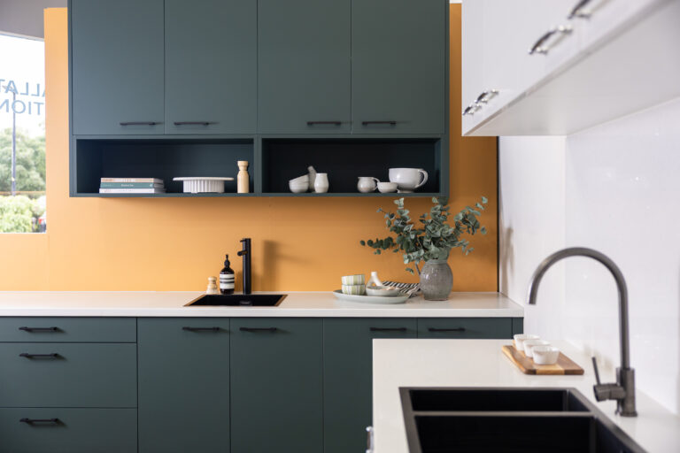 Green kitchen with burnt orange splashback with open shelving and decorative finishes in