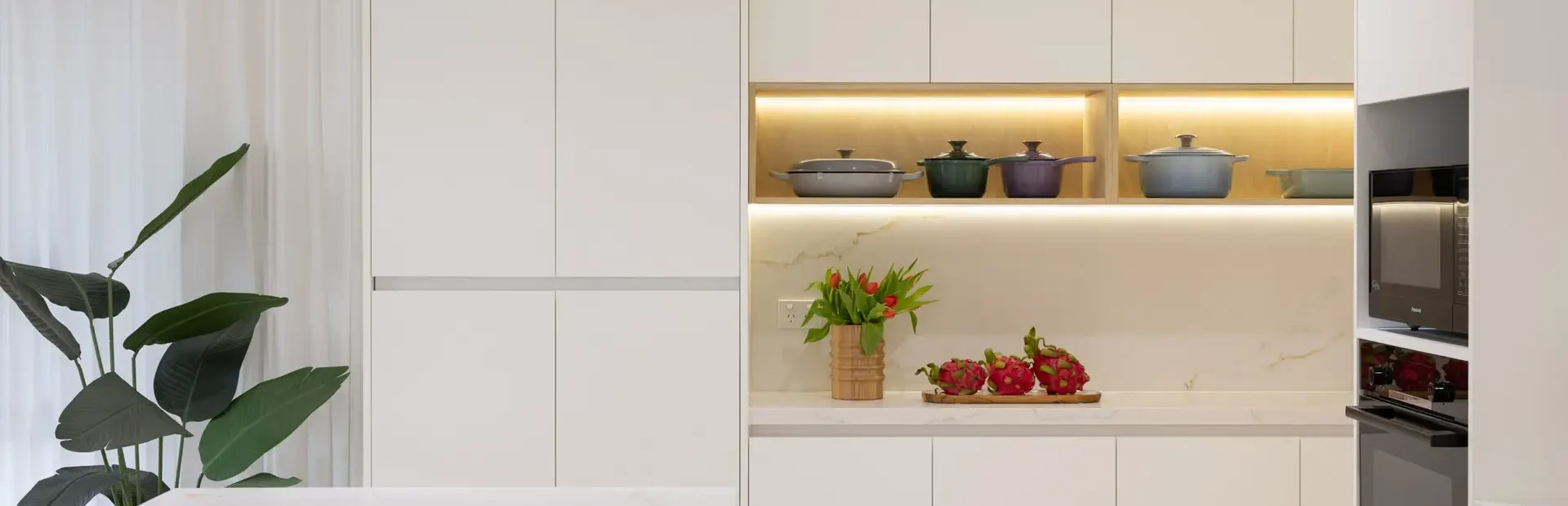 White handle free kitchen featuring white cupboards with timber feature shelving with styling pots and vase with flower