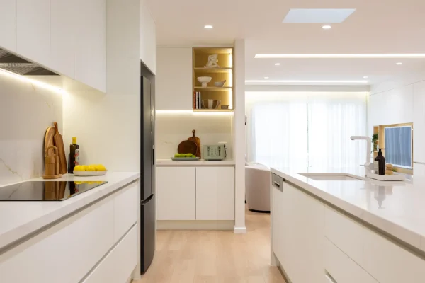 Galley style kitchen displaying white handleless cabinetry with black fridge dishwasher and nook at the end with toaster and kitchen styling items