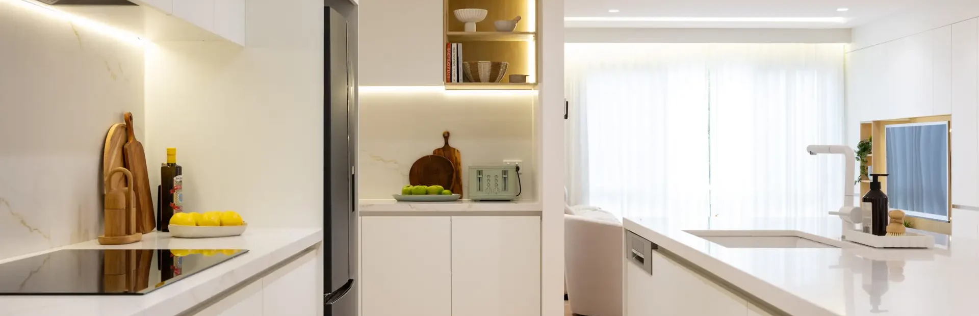 Galley style kitchen displaying white handleless cabinetry with black fridge dishwasher and nook at the end with toaster and kitchen styling items
