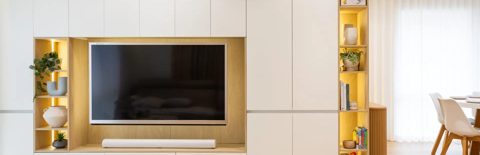Living room cabinetry displaying a large wall of handle free white and birch laminate cabinetry with styling items in open shelf at the end