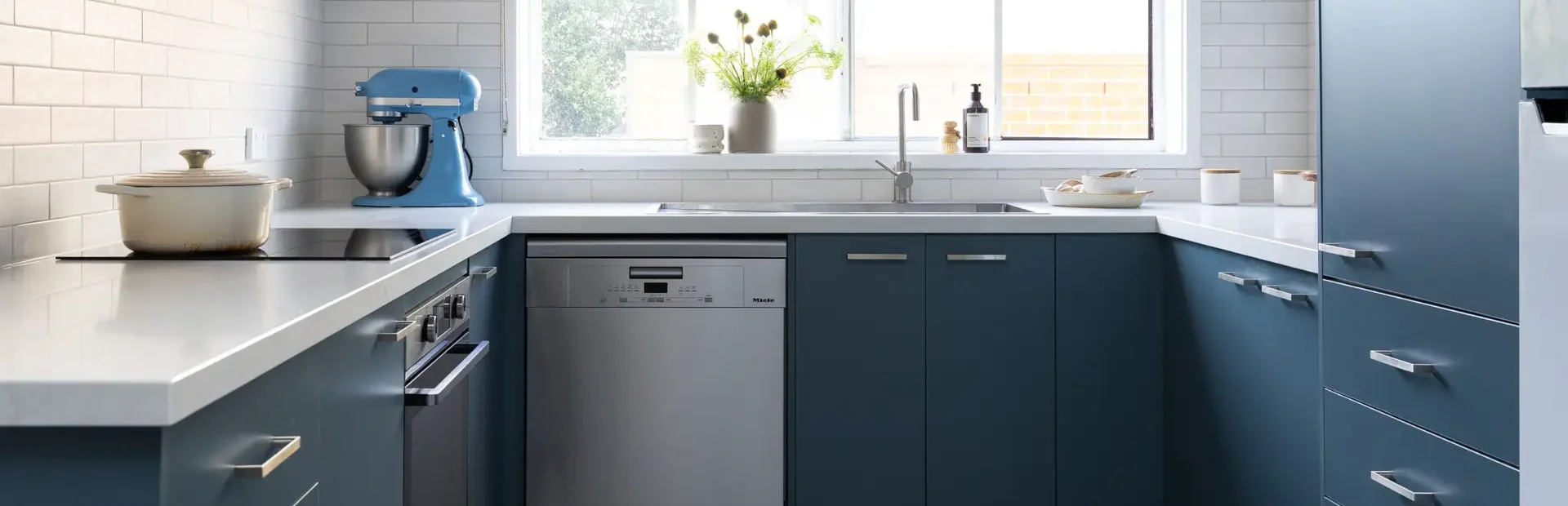 U shaped blue colour kitchen with chrome handles, dishwasher and induction cooktop with pot