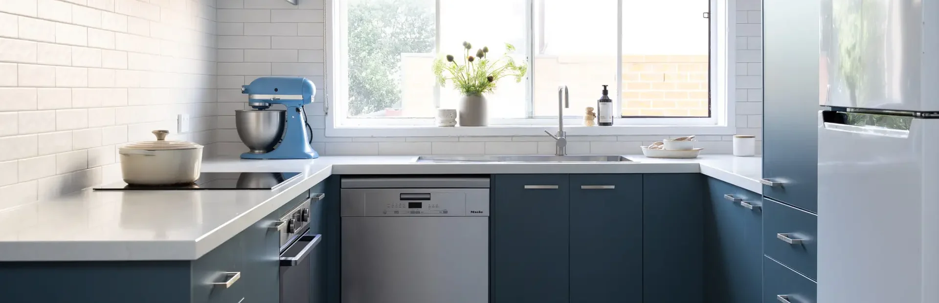 Blue colour kitchen cabinetry in u shape kitchen with blue mixmaster and cream pot on cooktop