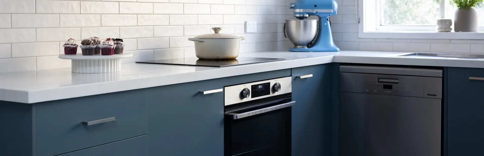 Kitchen with blue cabinetry displaying underbench oven and induction cooktop with mixmaster cakes and pot on cooktop
