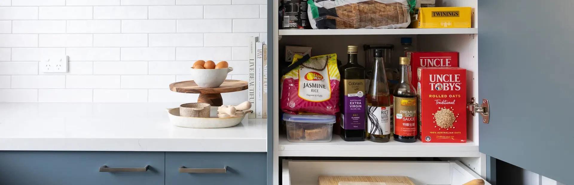 Kitchen featuring tall pantry with pantry items with blue cabinetry and white stone benchtops with eggs on bench