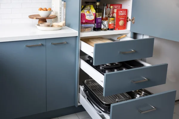Blue kitchen cabinetry featuring closed doors and open drawers with open pantry above with pantry items