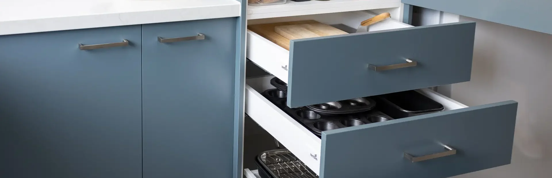 Blue kitchen cabinetry featuring closed doors and open drawers with open pantry above with pantry items