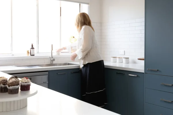 Female organising items in a blue u shape kitchen at the sink with open window