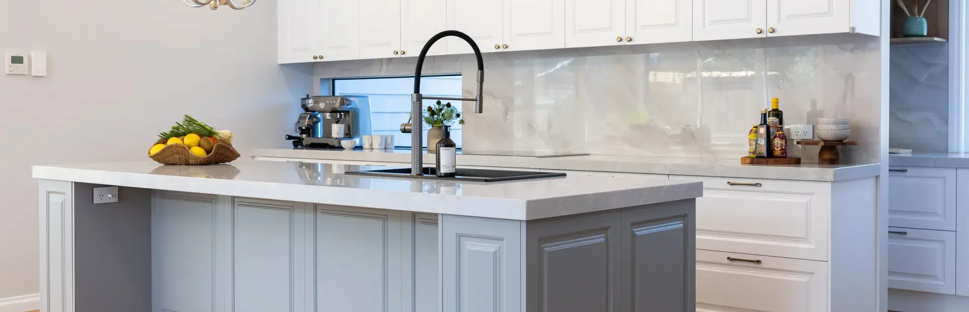 Carrington Shaker style kitchen with white cabinetry featuring grey large island with gooseneck tap and stone benchtops, gold pendant lights and herringbone timber flooring