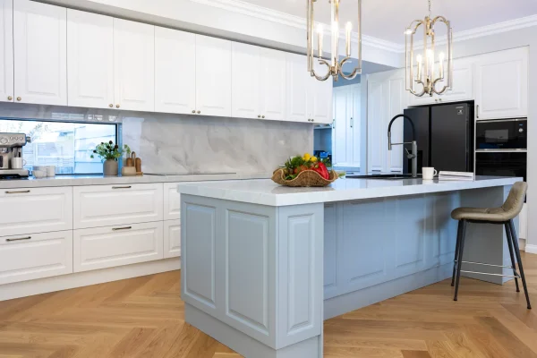 Carrington Shaker style kitchen with white cabinetry and grey featuring on large island bench with wicker basket with fruit on stone benchtops, gold pendant lights and herringbone timber flooring