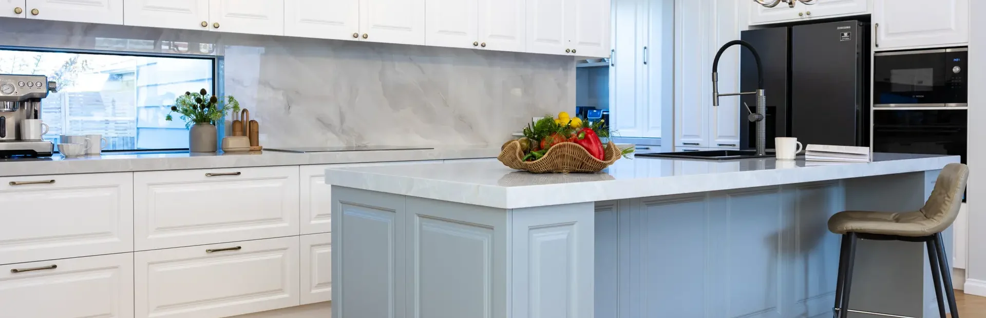 Carrington Shaker style kitchen with white cabinetry and grey featuring on large island bench with wicker basket with fruit on stone benchtops, gold pendant lights and herringbone timber flooring