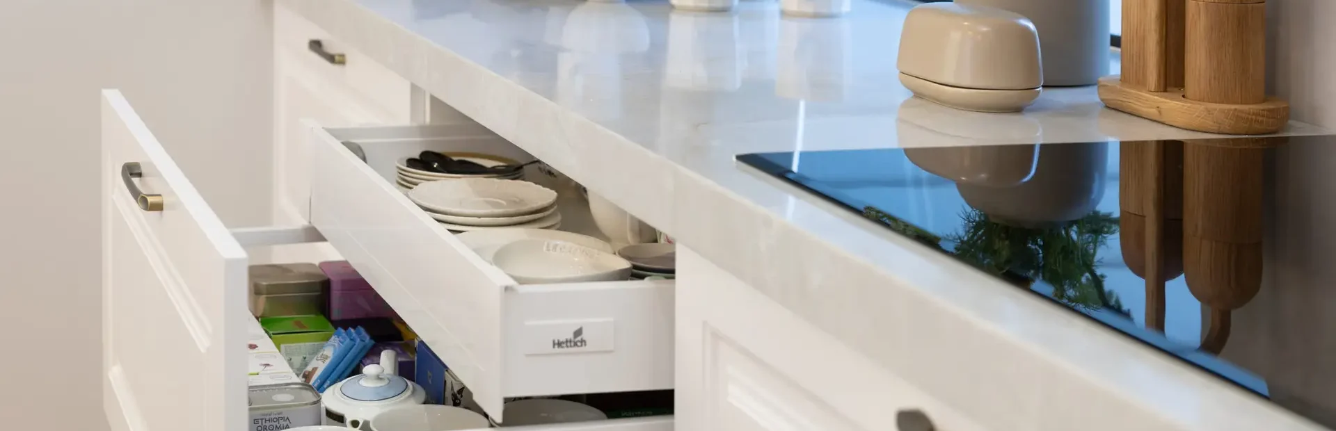 White carrington style kitchen cabinetry featuring drawers with inner concealed drawer with teas and cups, coffee machine on stone benchtop with coffee cups and country road vase of flowers with butter dish
