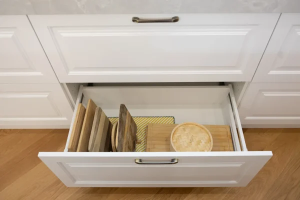 Kitchen cabinetry drawers featuring white recessed panels and timber chopping boards with bamboo steamer and chrome handles on cabinetry drawers