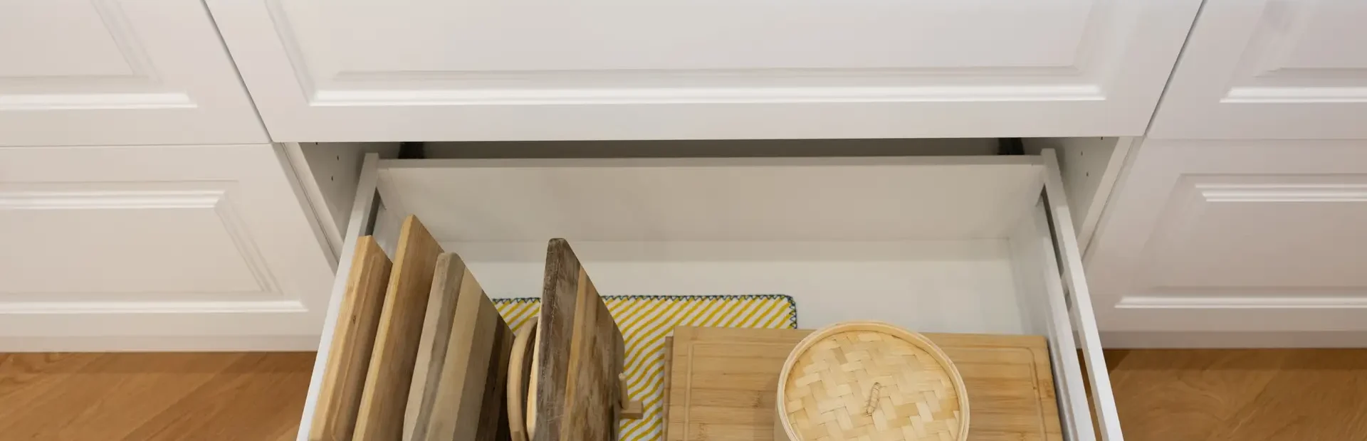 Kitchen cabinetry drawers featuring white recessed panels and timber chopping boards with bamboo steamer and chrome handles on cabinetry drawers