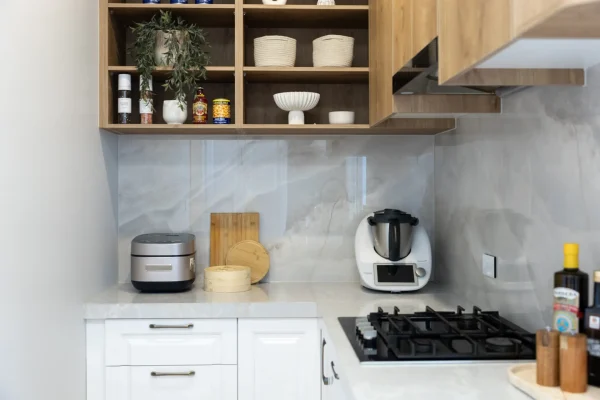 Butlers pantry featuring white kitchen cabinetry in shaker style with oak timber overheads and open shelving displaying styling items, thermomix on the benchtop with chopping boards and oils and black cooktop